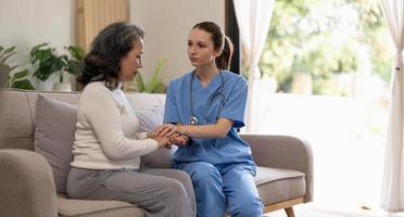 Happy patient is holding caregiver for a hand while spending time together. Elderly woman in nursing home and nurse. photo