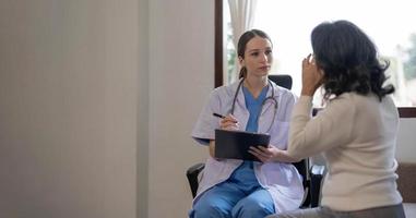 Asian female patient undergoing health check up while female doctor uses stethoscope to check heart rate in nurse, health care concept photo