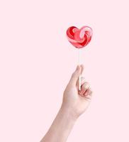 Heart shaped lollipop candy in hand isolated on pink background. photo