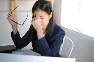 la mujer de negocios tiene dolor de ojos y dolores de cabeza. de trabajar frente a la computadora durante mucho tiempo. concepto de síndrome de oficina foto