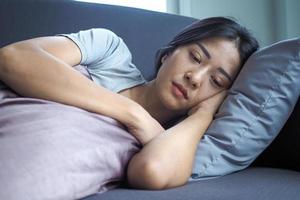 infeliz solitaria mujer deprimida en casa. ella está acostada en el sofá y escondiendo su rostro en una almohada, concepto de depresión foto