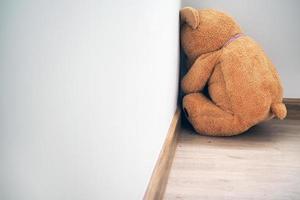 Child concept of sorrow. Teddy bear sitting leaning against the wall of the house alone, look sad and disappointed. photo