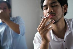 el hombre está fumando en la oficina. los colegas olieron cigarrillos y expresaron disgusto. foto