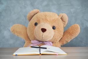 Teddy bear sit on the table and raise his hand photo