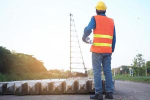 The engineer holds a blueprint in his hand, looking at the crane in the construction area. Building contractor concept photo