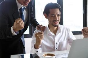 el gerente y el personal se veían felices mientras miraban la computadora en la mesa de reuniones. concepto de ganador foto