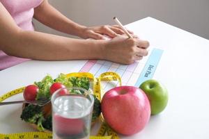 una niña sentada y escribiendo un plan de dieta concepto de pérdida de peso come alimentos que son buenos para el cuerpo. como frutas y verduras. foto