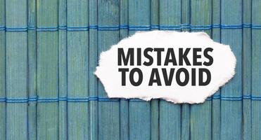 Mistakes To Avoid word on torn paper with blue wooden background photo