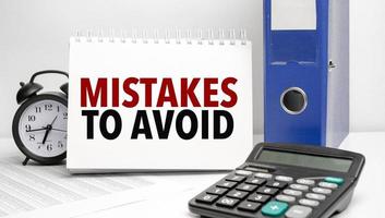Mistakes To Avoid words on white notebook and calculator, black vintage alarm clock and blue paper folder photo