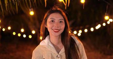 Aufnahmen einer asiatischen jungen glücklichen Frau, die in die Kamera schaut und mit hellem Bokeh-Hintergrund lächelt. party- und feierkonzept. Zeitlupe. video