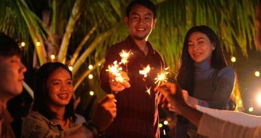 filmmaterial einer glücklichen asiatischen gruppe von freunden, die spaß mit wunderkerzen im freien haben - junge leute, die sich nachts mit feuerwerk amüsieren - menschen, essen, trinken, lebensstil, neujahrsfeierkonzept.