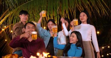 Filmmaterial von glücklichen asiatischen Freunden, die zusammen eine Dinnerparty haben - junge Leute, die am Bartisch sitzen und Biergläser zum Abendessen im Freien anstoßen - Menschen, Essen, Trinken, Lebensstil, Neujahrsfeierkonzept.
