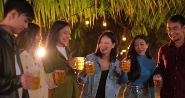 filmmaterial von glücklichen asiatischen freunden, die zusammen eine dinnerparty haben - junge leute, die biergläser zum abendessen im freien anstoßen - menschen, essen, trinken, lebensstil, neujahrsfeierkonzept.