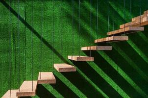 Hanging wooden stairs on artificial grass wall background Apartment staircase made of cables and wood apparently floating. photo