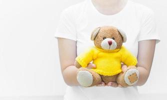 Woman holding and protecting give a brown Teddy Bear toy wear yellow shirts sitting on white background close-up,Symbol of love or dating photo
