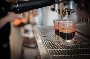 Primer plano de café negro en la taza medidora puesta en la cafetera, máquina de café haciendo espresso foto