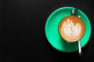 Hot latte in green cup with floral pattern in foam top view on a dark background photo
