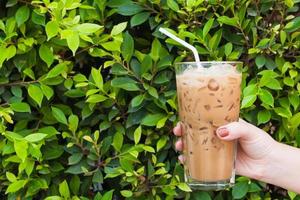 Hand woman holding the glass iced coffee on green nature background,Iced latte coffee photo