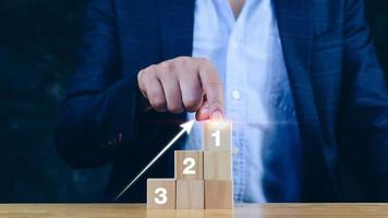 la mano del hombre de negocios elige el bloque de madera con el signo número 1 y la flecha hacia arriba, el concepto de éxito, ganador, victoria o clasificación superior. paso a paso foto