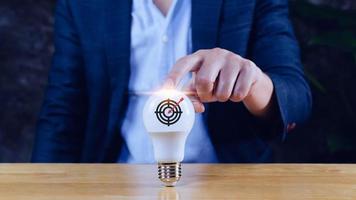 Businessman holding light bulb for concept new idea with virtual dartboard and arrow with copy space for setup business objective target concept. photo