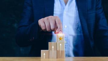 la mano del hombre de negocios elige el bloque de madera con el signo de la clasificación de estrellas formado garantía de calidad de servicio superior y flecha hacia arriba, garantía, concepto de estándares. foto