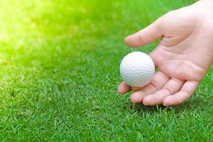 mano sosteniendo una pelota de golf sobre hierba verde con un primer plano de una pelota de golf con un enfoque suave a la luz del sol. parque deportivo para el concepto de club de golf foto