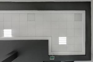 cassette stretched or suspended ceiling with square halogen spots lamps and drywall construction in empty room in house or office with column. Looking up view photo