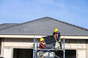 A team of Asian technicians installs solar panels on the roof of a house. Cross-section view of builder in helmet installing solar panel system concept of renewable energy photo