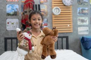 Sweet little girl is hugging a teddy bear, looking at camera and smiling while sitting on her bed at home. photo