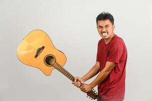 retrato de un joven asiático con una camiseta roja con una guitarra acústica aislada de fondo blanco foto