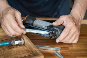 carpenter using nail gun or brad nailer tool ,load a top loading stapler  in a workshop ,furniture restoration woodworking concept. selective focus photo