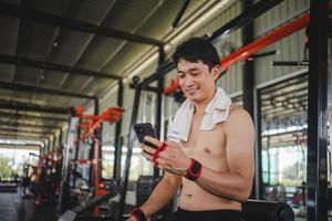 young male playing phone and listening to music after exercise with various exercise equipment in fitness. photo