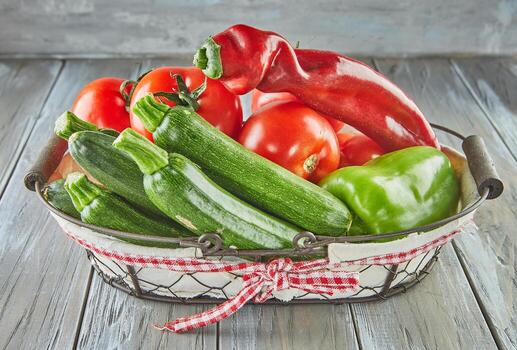 Zucchini, bell pepper, tomatoes and Red Italian heirloom pepper in basket on wooden background photo