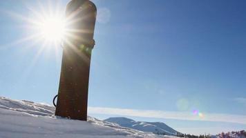 Black snowboard in snow with Beautiful mountains and fresh snow particles. Winter ski resort off piste background. Close up texture. Backcountry snowboarding video