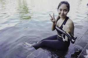 Attractive young woman sitting by the edge of a swimming pool, holding a google photo