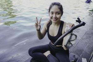 Attractive young woman sitting by the edge of a swimming pool, holding a google photo