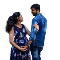 Indian couple posing for maternity baby shoot with white plain background. The couple is posing in a lawn with green grass and the woman is falunting her baby bump in Lodhi Garden in New Delhi, India photo