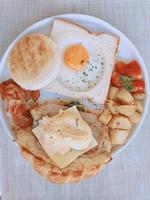 desayuno casero: huevos fritos, tocino, jamón, tomates, queso, papas y tostadas, vista superior. foto