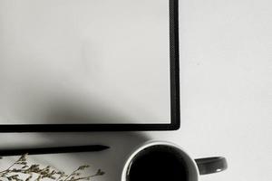 Top view of minimal workspace with blank screen , book, a cup of coffee, glasses, pen on white color desk. photo