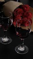 cena romántica. dos copas de vino tinto en el escritorio negro, ramo de flores sobre la mesa, enfoque selectivo en el ramo de rosas foto
