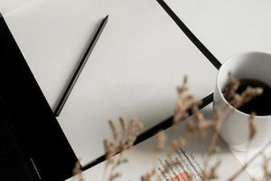 Top view of minimal workspace with blank screen , book, a cup of coffee, glasses, pen on white color desk photo