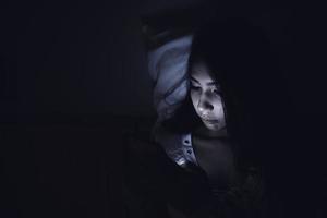mujer asiática juega al teléfono inteligente en la cama por la noche, gente de tailandia foto