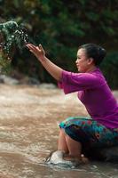 Happy Asian woman playing with the water near the river while sitting on the rock and wearing a purple dress photo