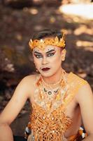 Balinese man with eyeshadow and black lipstick on his face while wearing a golden costume and crown photo