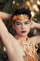 sexy Balinese man shirtless in makeup while wearing a golden crown and golden accessories with black hair photo