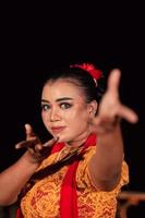 A Balinese woman poses with both her hands in a traditional orange dress and red scarf on her body photo