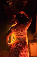 A Silhouette body of a Balinese woman in a traditional orange dress while dancing in front of the lighting on the dark night photo