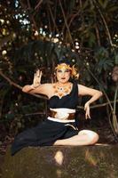 Indonesian woman sitting on the rock in a black dance costume while wearing a golden crown and golden necklace photo