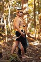 A Tribal Man poses with makeup on her face while wearing gold accessories on his head and neck photo