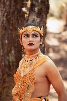 A Manly Asian man poses with a golden crown and gold costume while standing in front of the tree photo